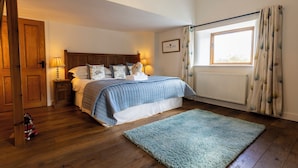 Een slaapkamer met een houten vloer, een bed met een blauw-witte dekbedovertrek, twee bedlampen, een raam met gordijnen en een radiator.