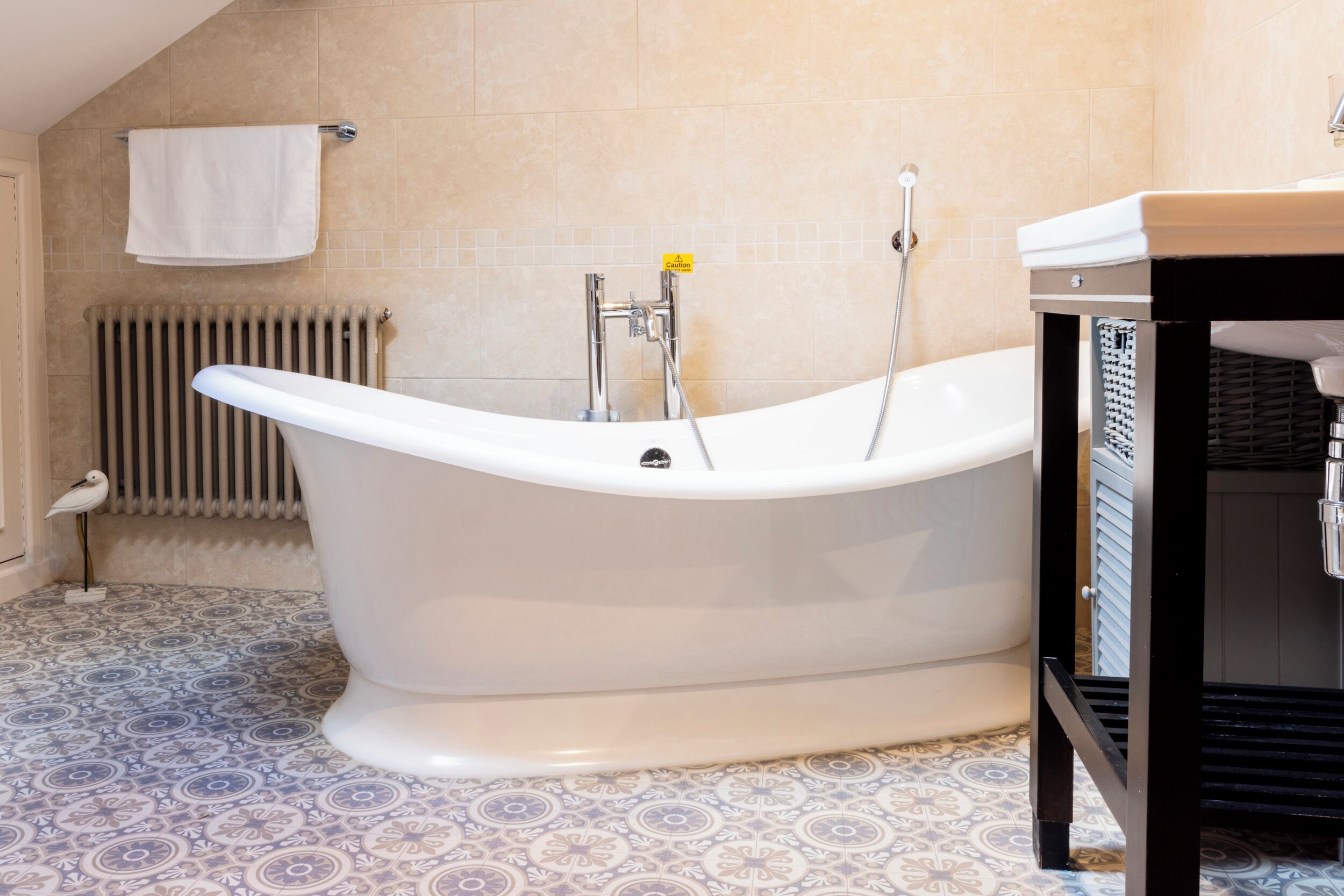 A bathroom with a freestanding bathtub, a radiator, patterned floor tiles, and a towel rack.