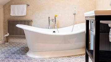 A bathroom with a freestanding bathtub, a radiator, patterned floor tiles, and a towel rack.