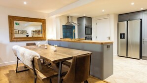 Een moderne keuken met een houten eettafel, bruine stoelen, een geïntegreerd kookeiland met een spoelbak en roestvrijstalen apparatuur.