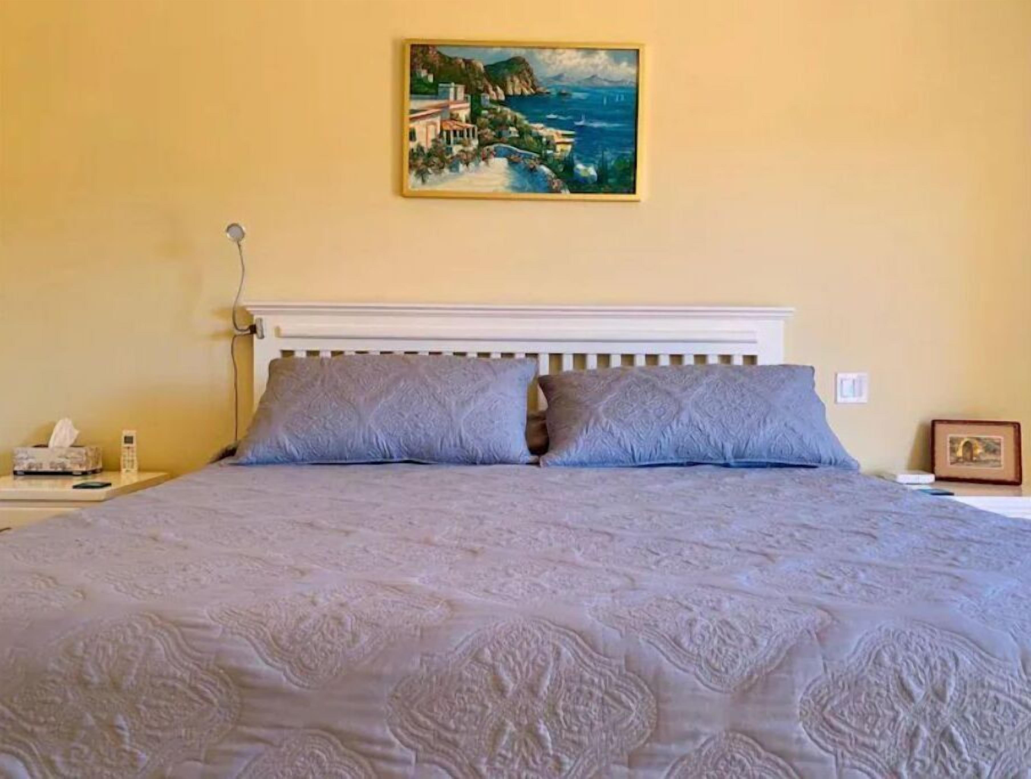 Ein Bett mit weißem Kopfteil, zwei Kissen und ein Gemälde einer Küstenlandschaft an der Wand.