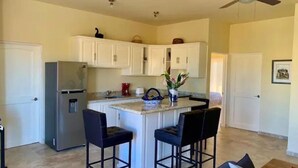 A compact kitchen with white cabinets, a refrigerator, and a small island with two bar stools. - 3B Cerritos Beach Condo, Lrg Pool, Baja Sur (El Pescadero)