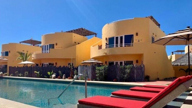 A pool area with a checkered floor, red lounge chairs, and a building with multiple balconies. - 3B Cerritos Beach Condo, Lrg Pool, Baja Sur (El Pescadero)