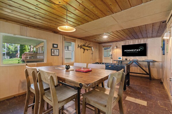 A wooden-floored dining area with a large table, chairs, and a foosball table.