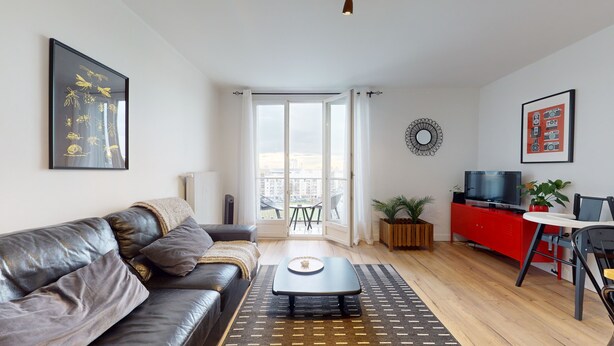 Una sala moderna con un sofá de cuero, una mesa de centro, un mueble rojo con un televisor y un balcón con vistas a la ciudad.