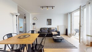 Una sala moderna con un sofá de cuero negro, una mesa de comedor de madera y una mesa de centro negra. Hay una lámpara de pie negra, un cuadro en la pared y un radiador.