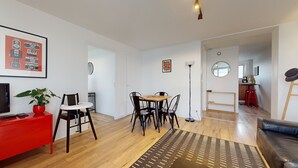 Una sala moderna con comedor, un mueble de entretenimiento rojo, una planta en maceta y un sofá de cuero negro.