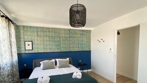Un dormitorio moderno con cama, mesita de noche, lámpara colgante y puerta que da a otra habitación.
