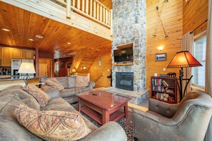 L’intérieur d’une cabane en rondins, avec une cheminée en pierre, un plafond en bois et un coin salon accueillant.