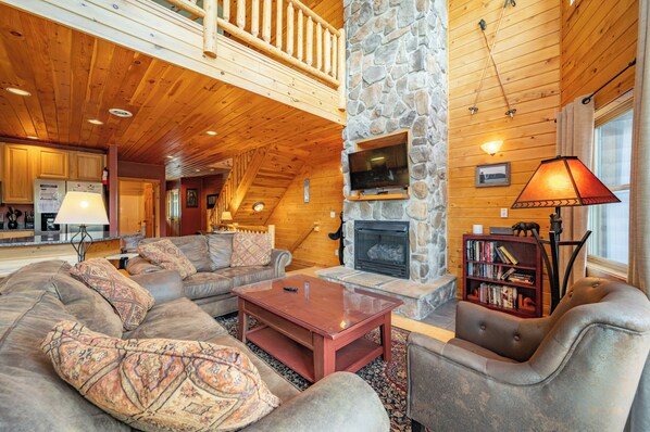 A log cabin interior with a stone fireplace, wooden ceiling, and a cozy seating area.