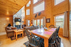 L’intérieur d’un chalet en bois comprend une cheminée en pierre, une table à manger avec des chaises, un canapé et un téléviseur.