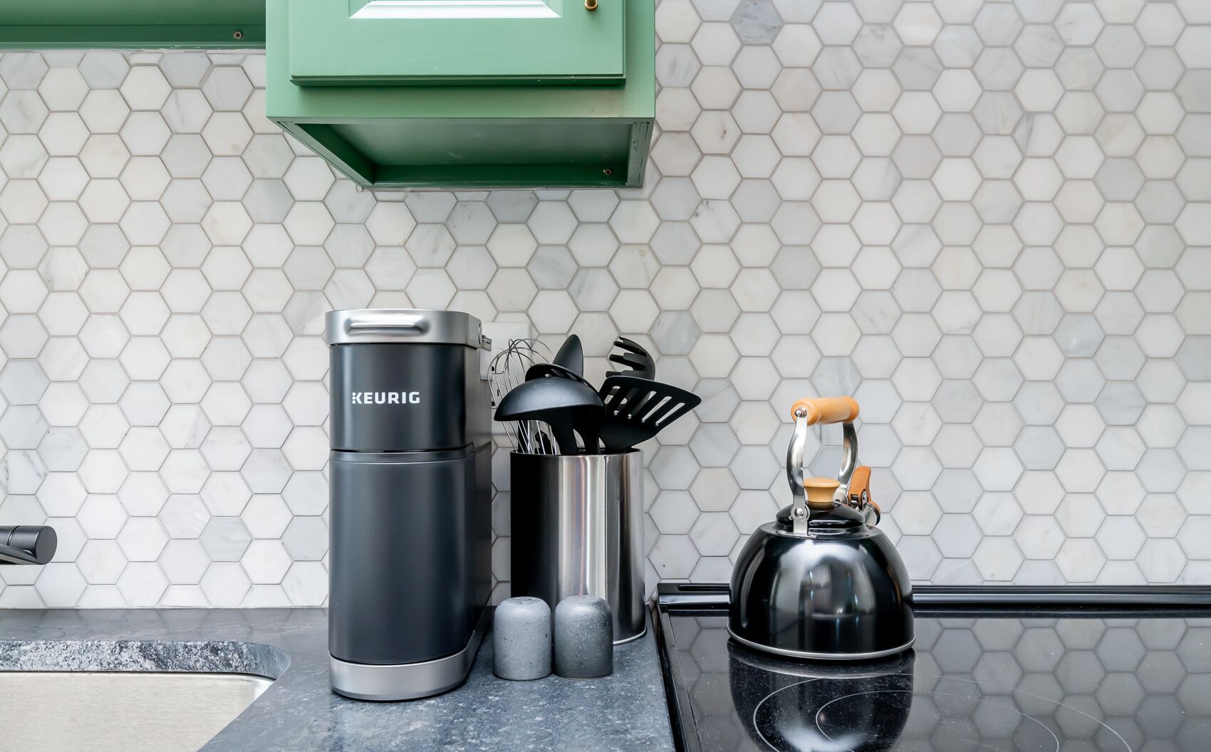 Uma cozinha com painel de azulejos hexagonais, uma cafeteira Keurig, um bule e um saleiro.