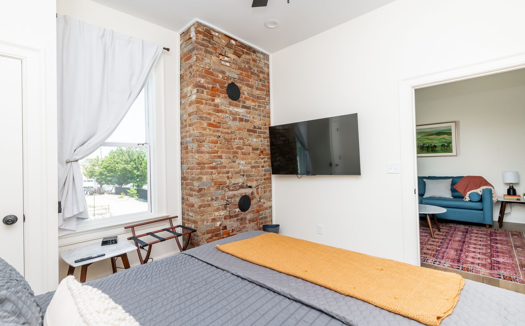 Une chambre avec un mur en briques, un lit, une télévision et une vue sur l’extérieur.