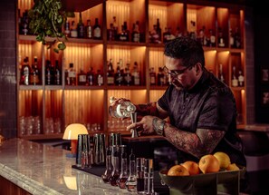 A bartender preparing drinks at a bar with a well-stocked liquor shelf in the background. - Double Pour @Tartan House - 2 Suites in 1 Sleep 10 (Louisville)