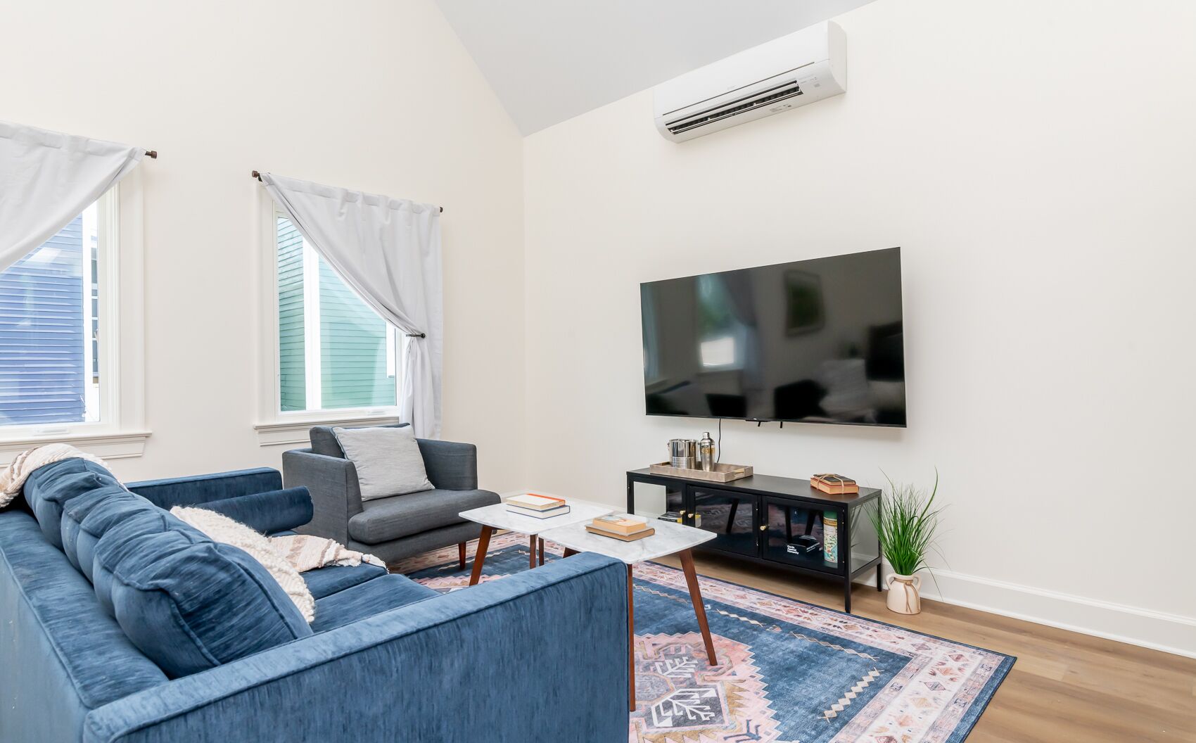 Una sala moderna con un sofá azul, un sillón gris, una mesa de centro y un televisor de pantalla plana montado en la pared.