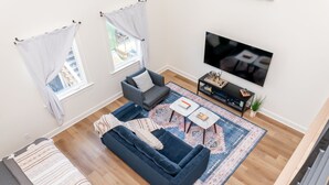 A modern living room with a dark blue sofa, a small coffee table, and a TV mounted on the wall. - Rickhouse Loft @Tartan House - Studio+Loft Sleep 6 (Louisville)