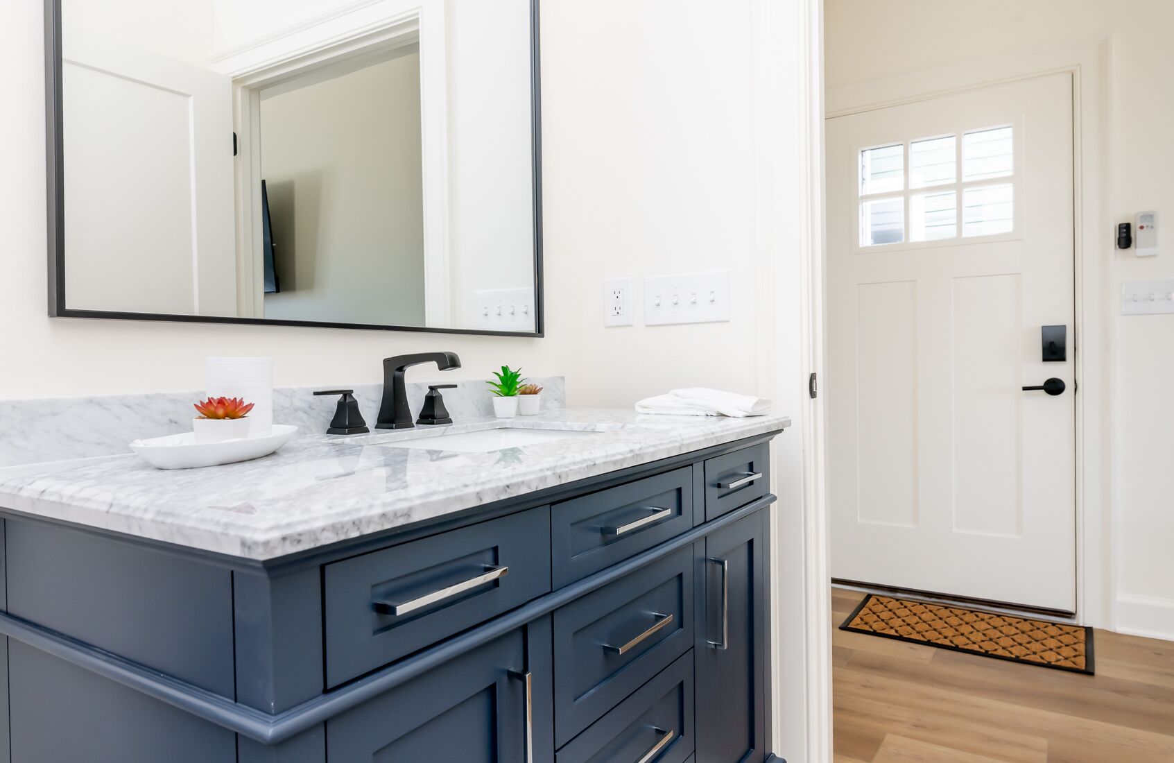 A bathroom with a marble countertop, dark blue cabinets, a large mirror, and a white door.