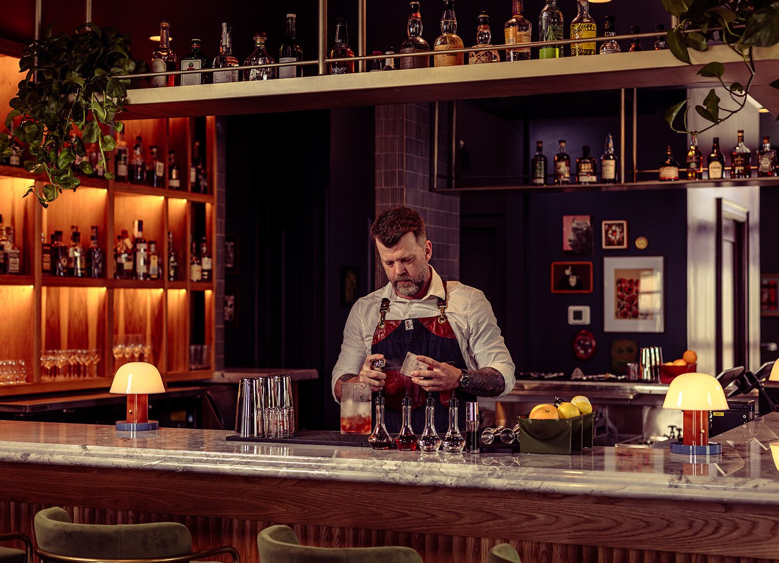 Un bar con estantes llenos de botellas de licores, un barman preparando bebidas y taburetes.