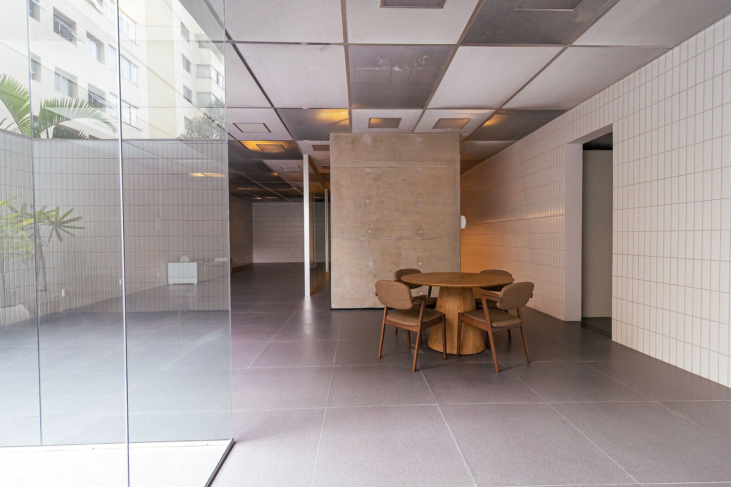 A modern interior with a glass partition, a round wooden table with chairs, and tiled walls.