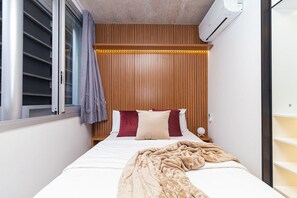 A bedroom with a bed, a window with curtains, an air conditioning unit, and a bedside table with a lamp. - Vossa Bossa Chez Frei (São Paulo)