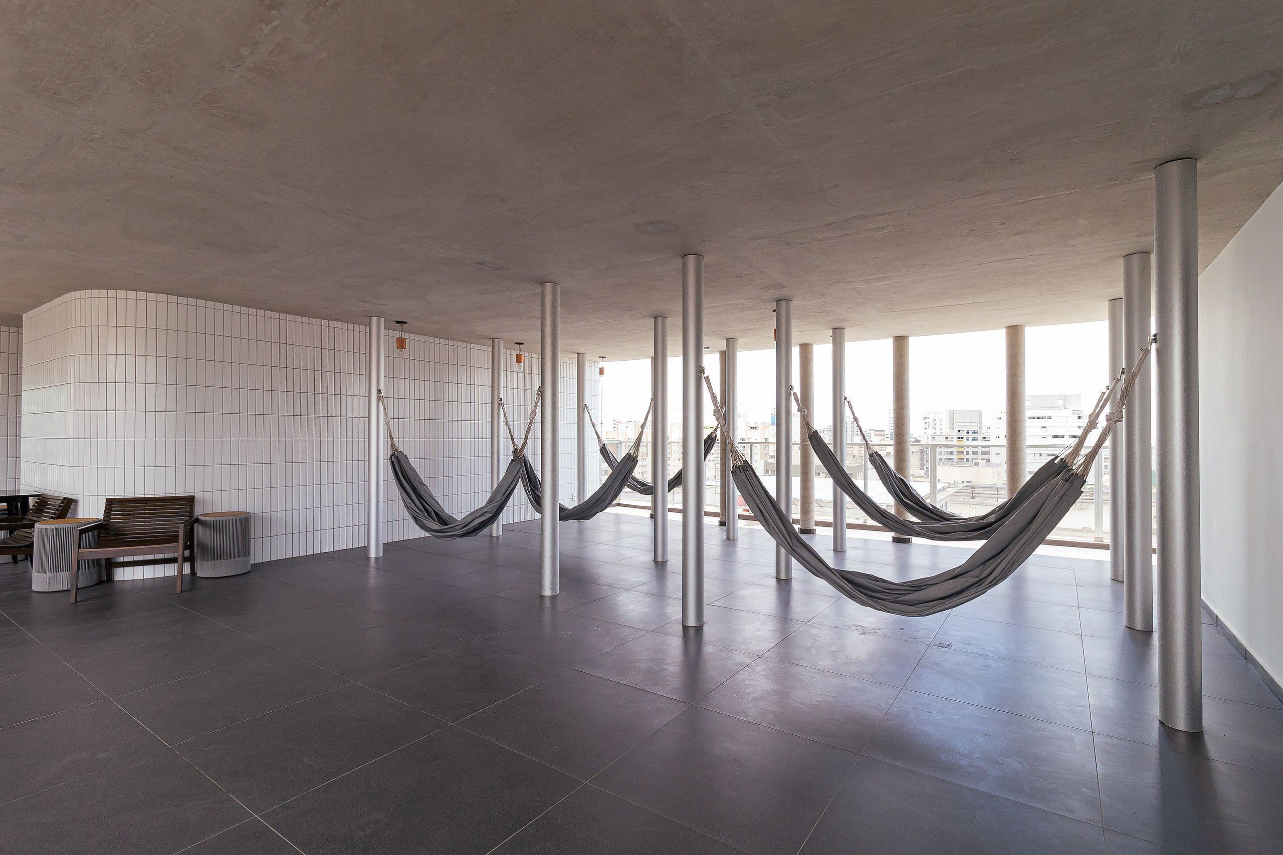 A spacious room with a tiled floor, a wooden bench, and several hammocks hanging from metal poles.