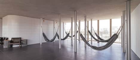 A spacious room with a tiled floor, a wooden bench, and several hammocks hanging from metal poles.