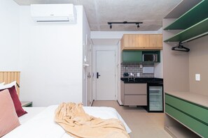 Una habitación compacta con cama, mesita de noche, microondas y una pequeña kitchenette.