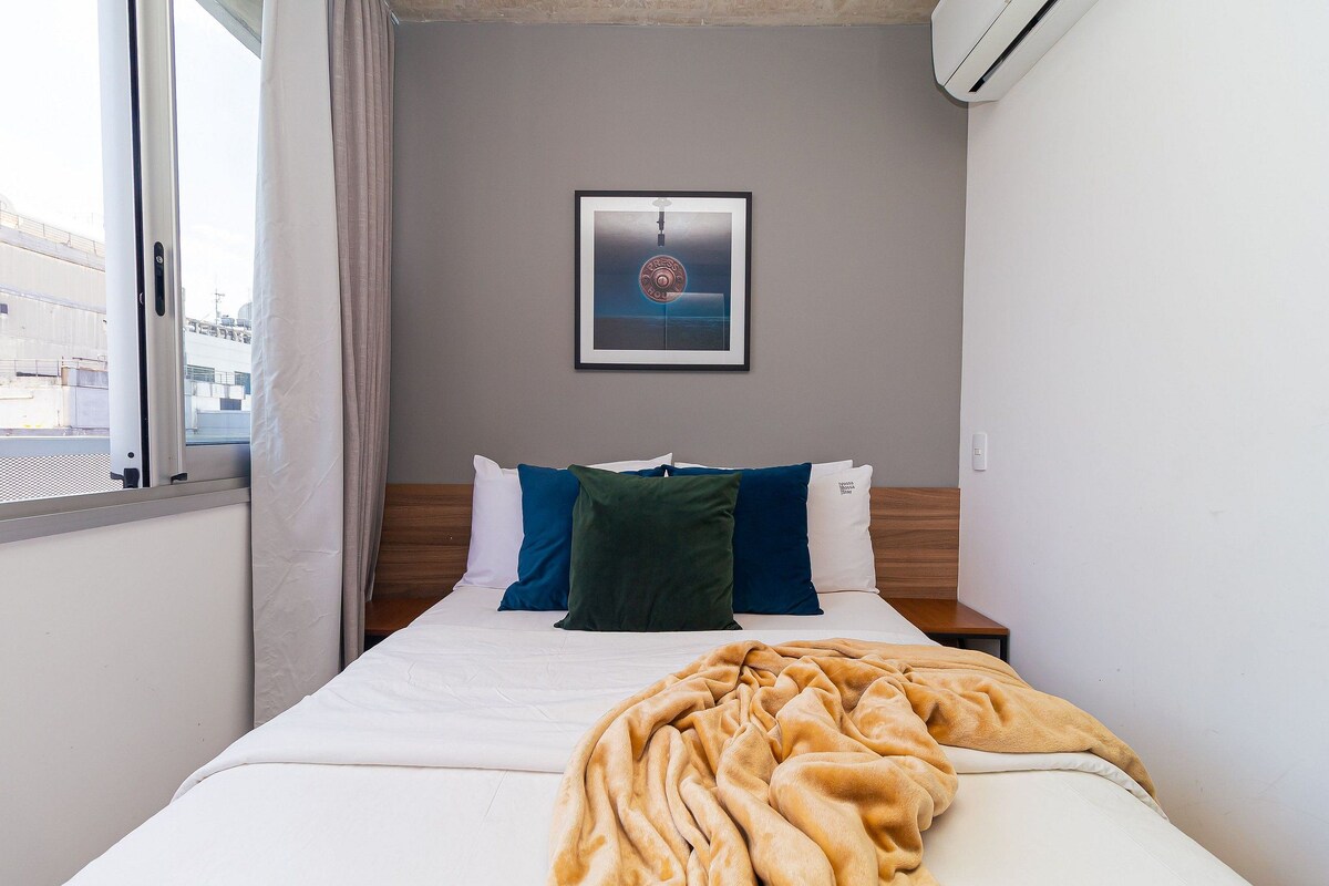 Habitación de hotel con cama, un cuadro en la pared y ventana con cortinas.