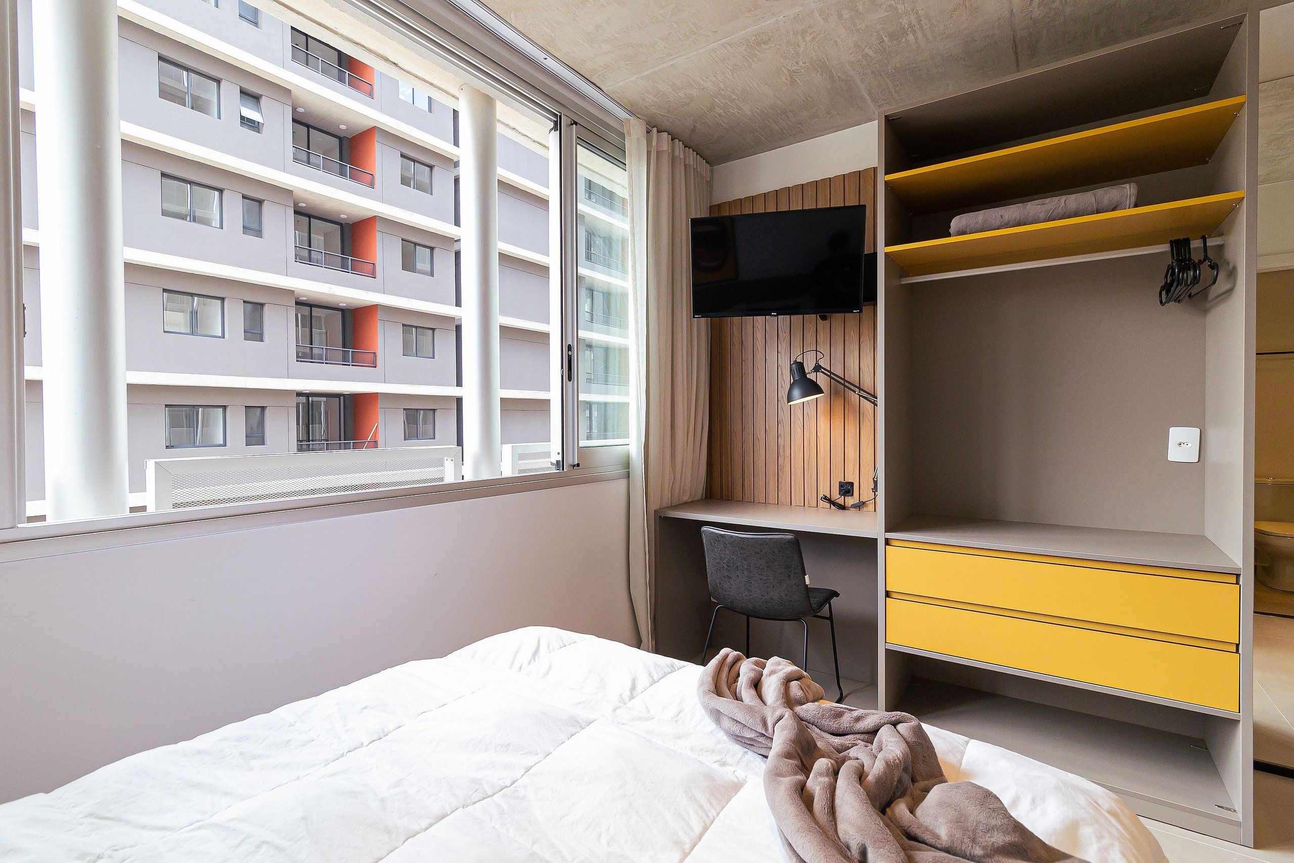 A bedroom with a bed, a desk, a chair, a TV, and a wardrobe.