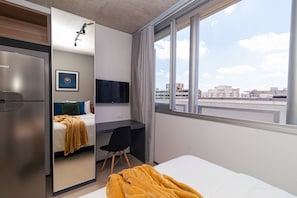 A modern hotel room with a bed, desk, and a large window offering a city view. - Vossa Bossa Chez Frei (São Paulo)