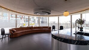 A modern lounge area with a curved sofa, a marble counter, and large windows offering city views. - Vossa Bossa Chez Frei (São Paulo)
