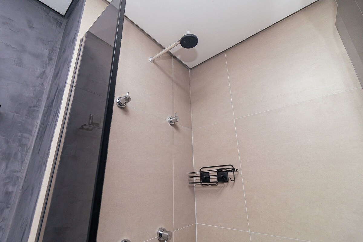 Una ducha moderna con cabezal de ducha manual, toallero en la pared y zona de ducha con mampara de vidrio.
