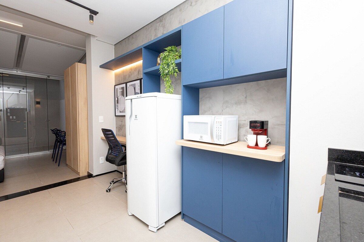 Una cocina moderna con un refrigerador blanco, un microondas y una cafetera sobre un estante azul.