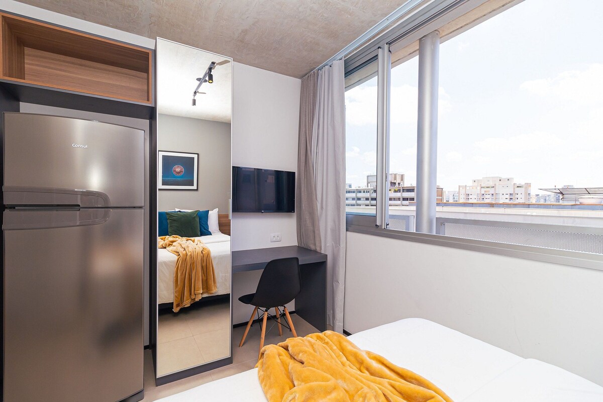 Une chambre d’hôtel moderne équipée d’un lit, d’un bureau, d’une télévision et offrant une vue sur la ville grâce à de grandes fenêtres.