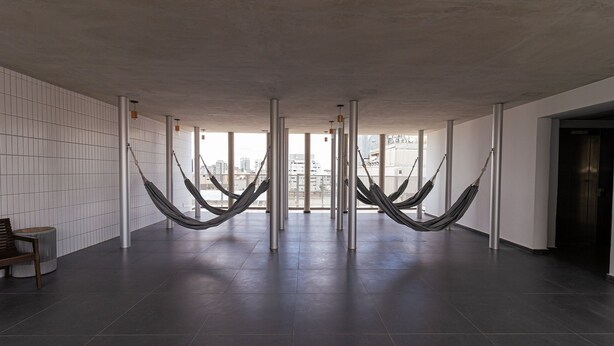A spacious lobby with a tiled floor, a bench, and hammocks hanging from the ceiling. - Vossa Bossa Chez Frei (São Paulo)