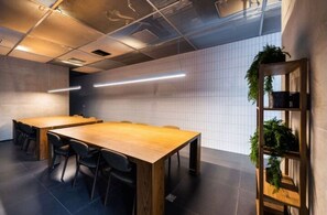 Une salle de conférence avec une longue table en bois, des chaises noires et un mur recouvert de carreaux blancs.