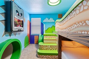 Una sala de juegos infantil con una cama, un televisor y una ventana.