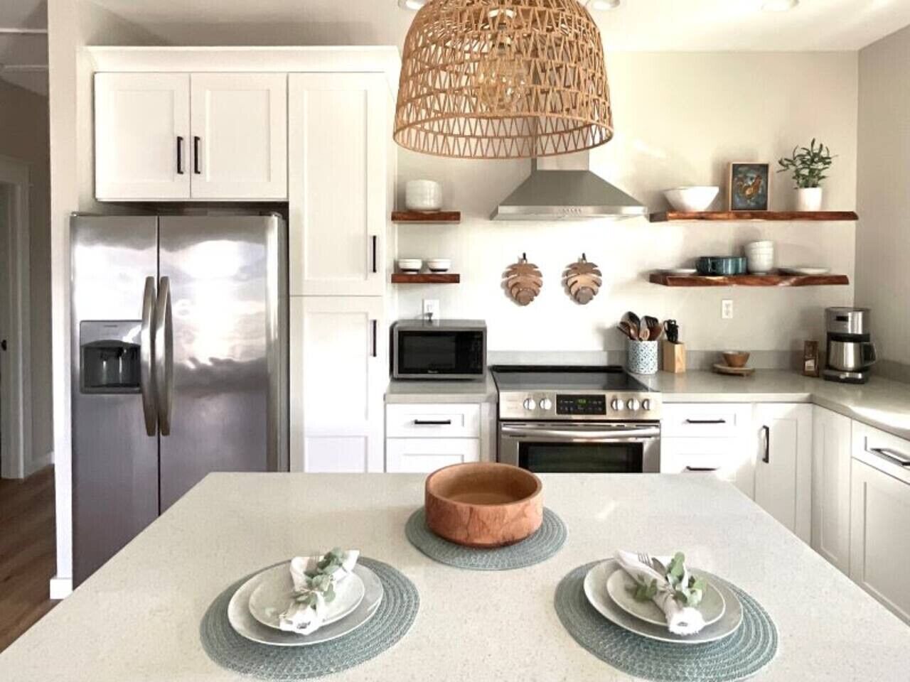 A modern kitchen with white cabinets, stainless steel appliances, a central island with a wooden bowl, and decorative wall art.