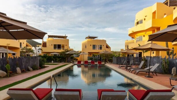 A pool area with lounge chairs and umbrellas, surrounded by yellow buildings.