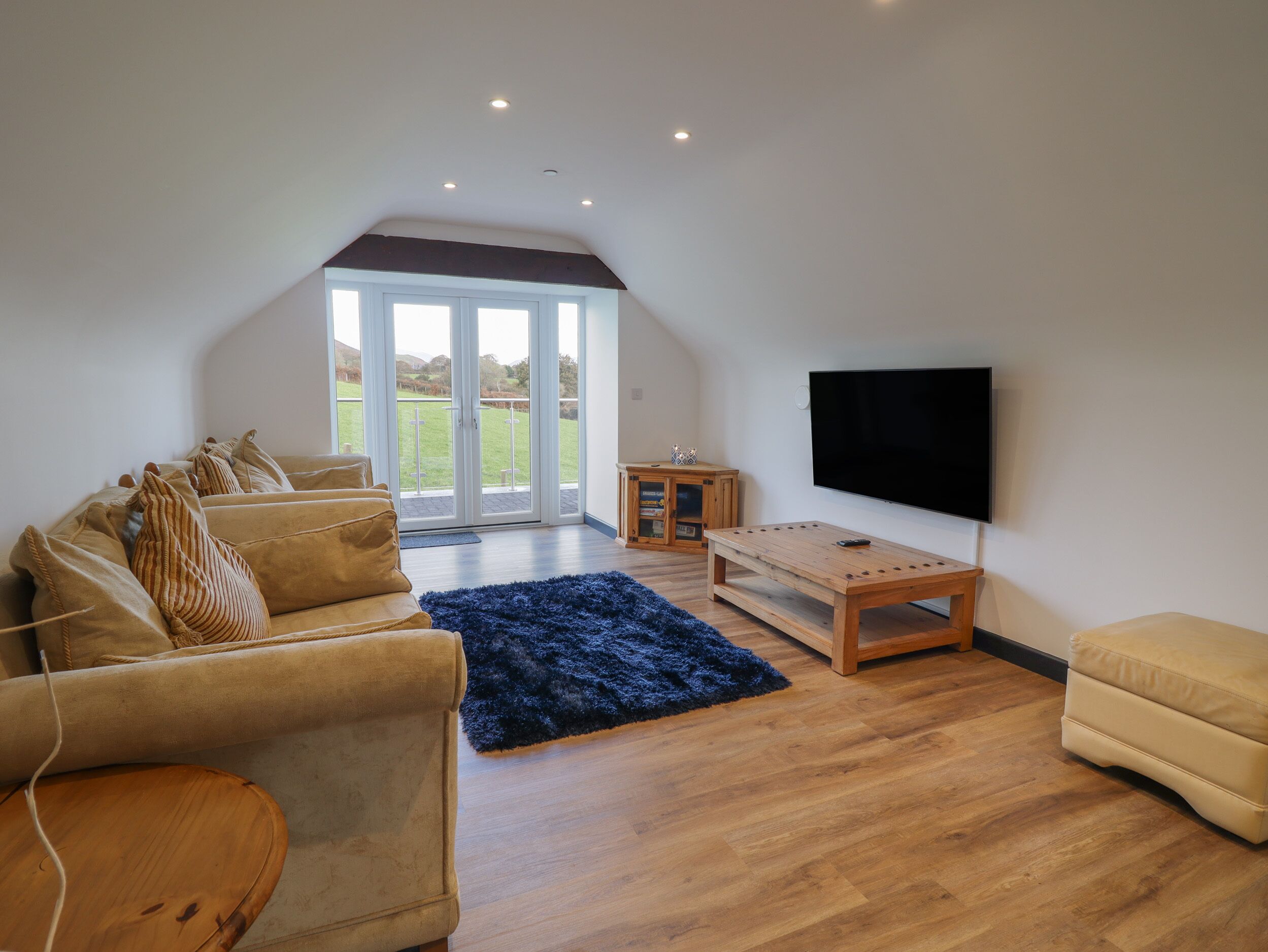 A spacious living room with a high ceiling, a large TV, a wooden coffee table, a sofa, and a view through a glass door to the outdoors.