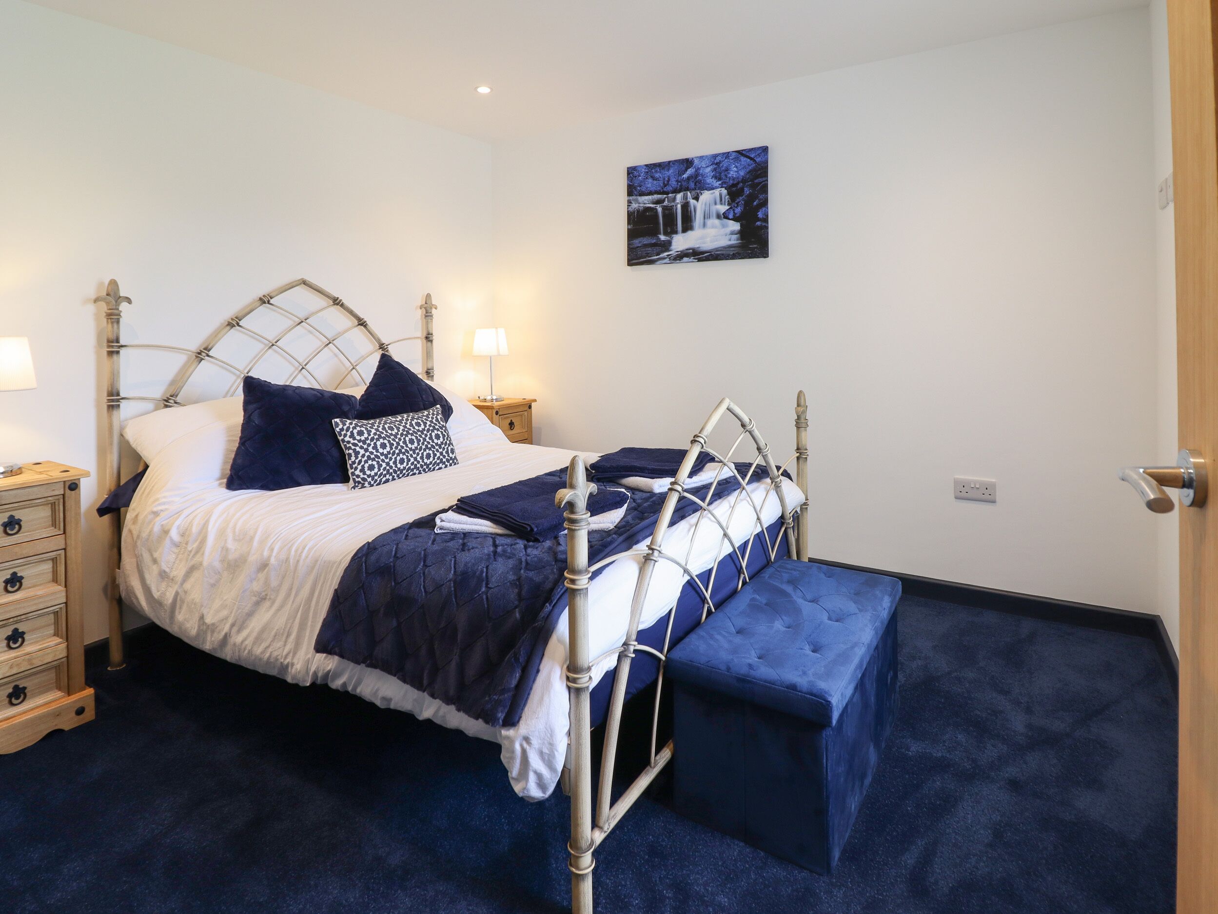 A neatly arranged bedroom with a metal-framed bed, a bedside table with a lamp, and a bench at the foot of the bed.