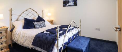 A neatly arranged bedroom with a metal-framed bed, a bedside table with a lamp, and a bench at the foot of the bed.