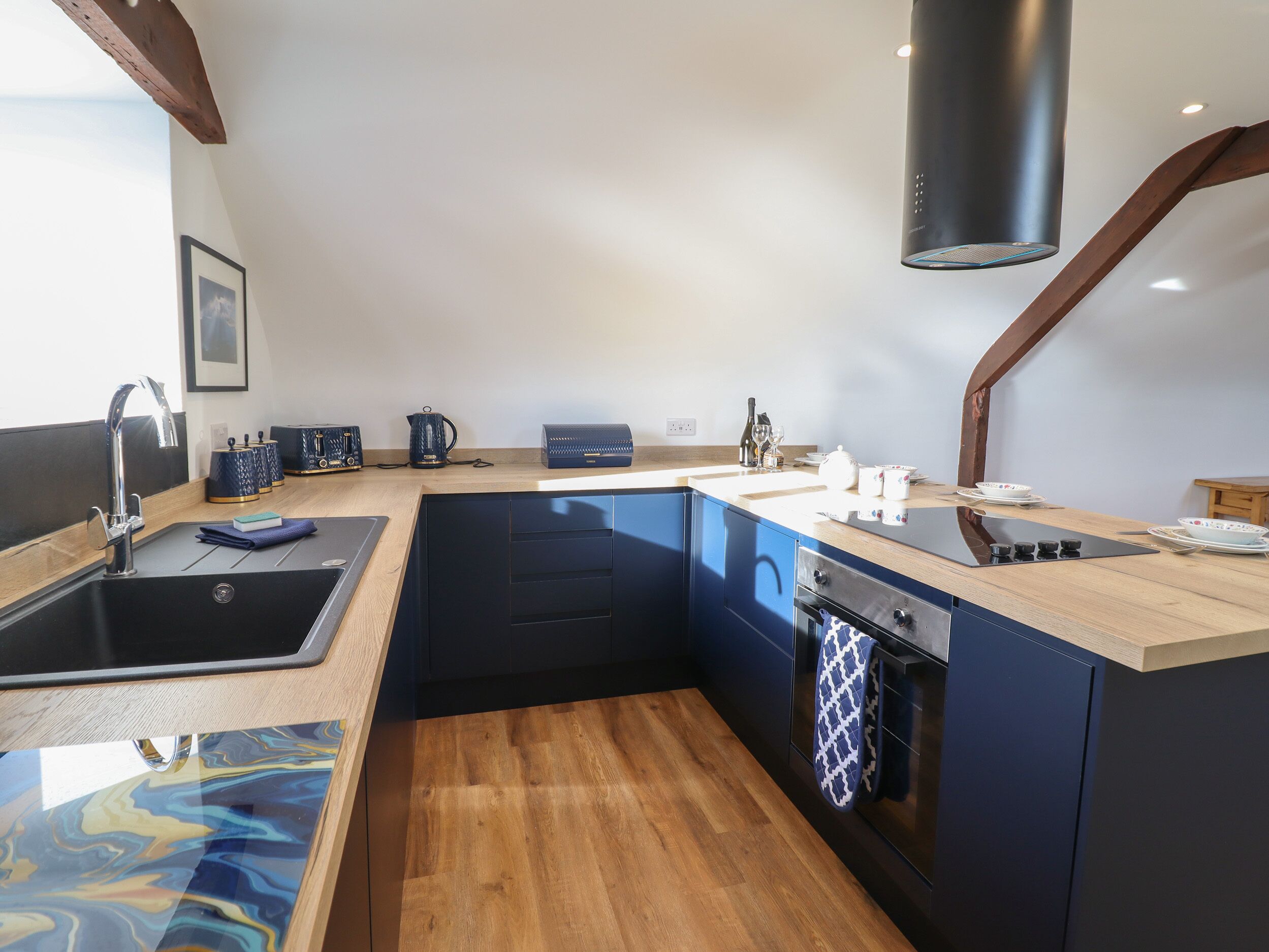 A modern kitchen with a wooden countertop, black cabinets, a built-in oven, and a stainless steel sink.
