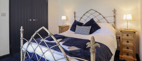 A neatly made bed with a headboard, two bedside tables with lamps, and a dark-colored wardrobe.