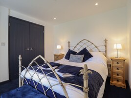 A neatly made bed with a headboard, two bedside tables with lamps, and a dark-colored wardrobe.