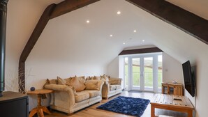 Ein gemütliches Wohnzimmer im Loft-Stil mit hohen Decken, Holzbalken, einer Sofagarnitur, einem kleinen Tisch und einem an der Wand befestigten Fernseher.
