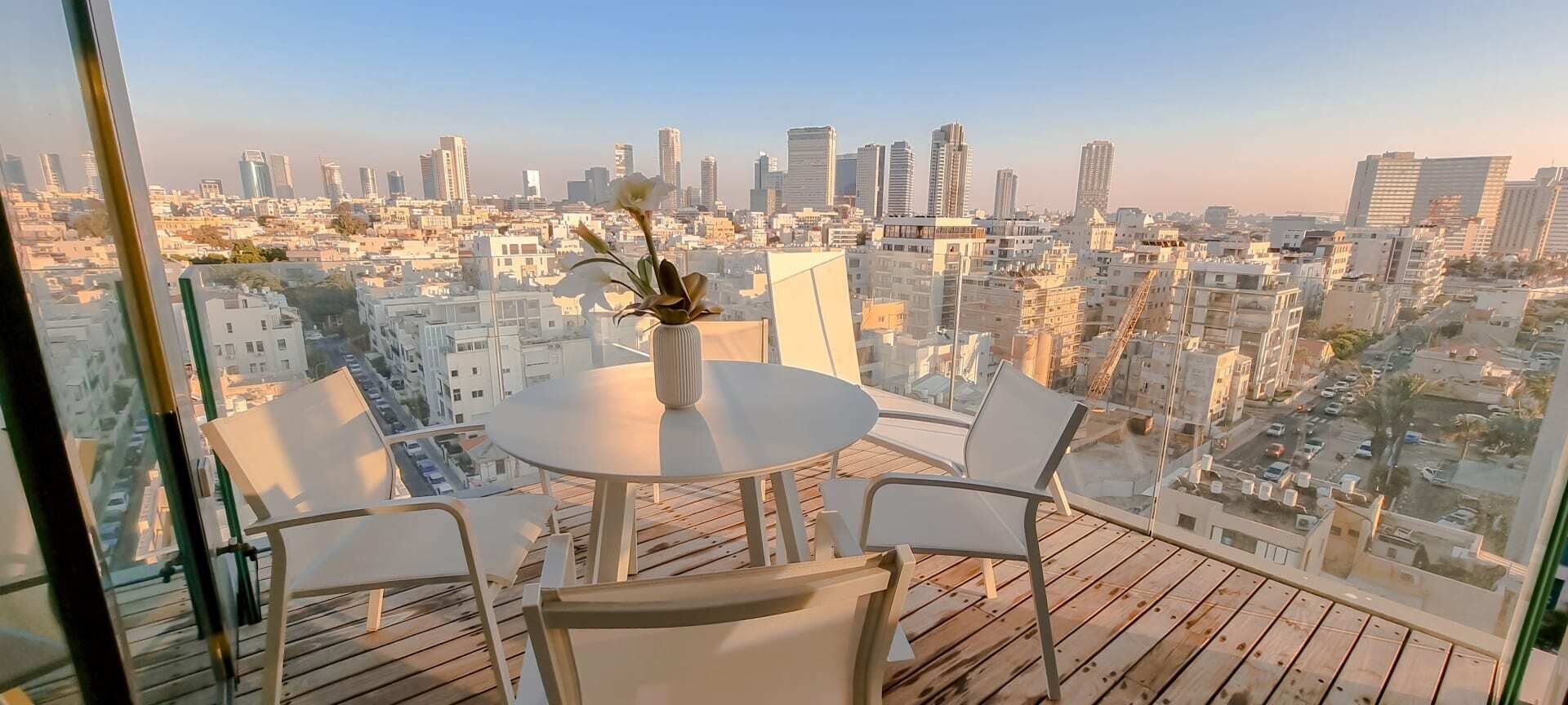 A balcony with a table and chairs, a vase with flowers, and a cityscape view.