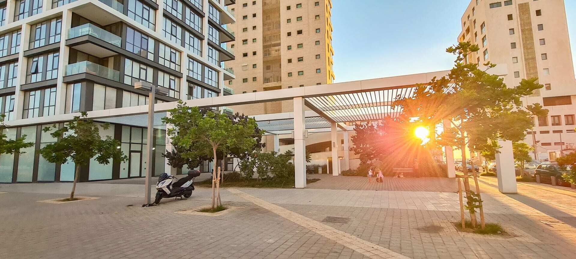 A modern building complex with multiple high-rise structures, a covered pedestrian area, and a few trees.