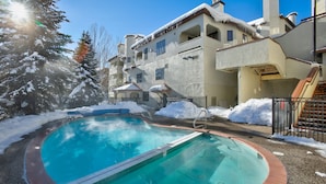 Una piscina amb vora de maó, envoltada de neu i un edifici amb balcons.