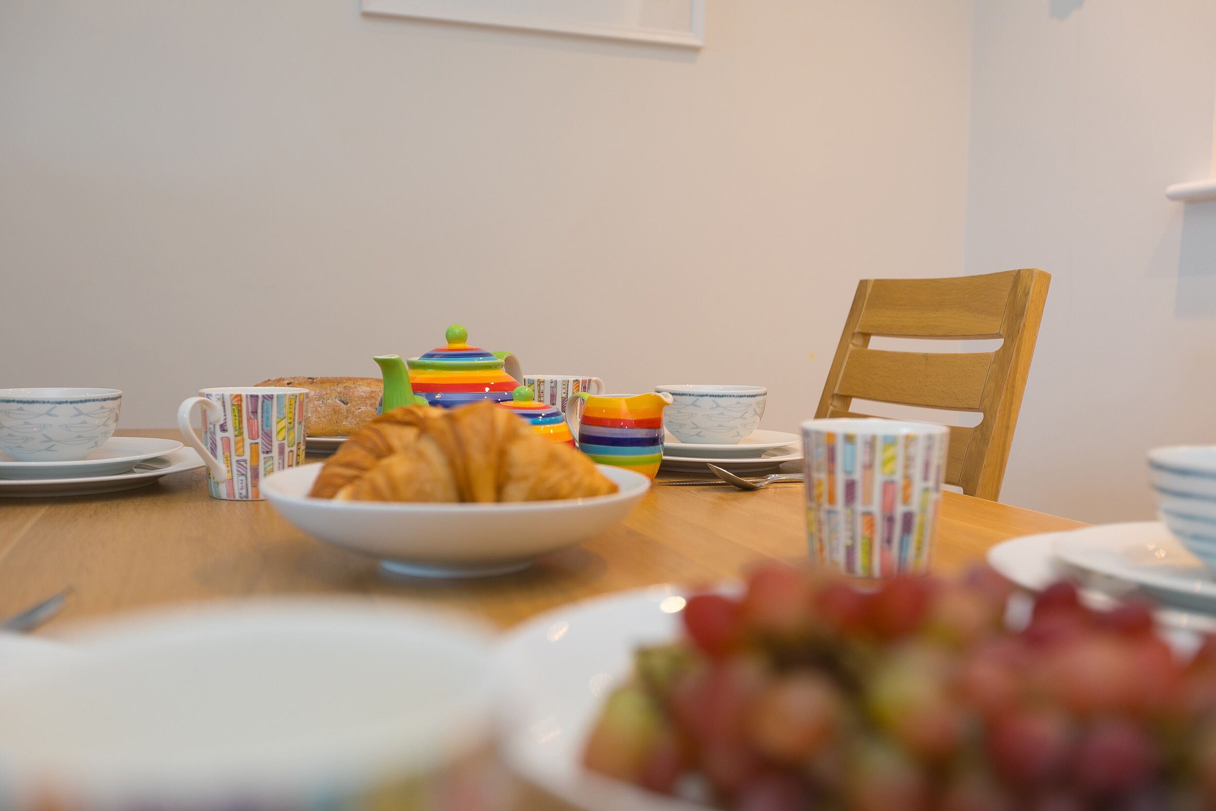 Une table à manger avec un croissant, des tasses colorées et une théière.